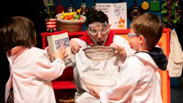 Colourful stage set of a restaurant kitchen filled with props and playful chaos